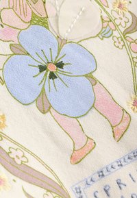 Blumiger Stoff mit einer großen hellblauen Blume, rosa Akzenten, grünen Blättern und aufwendigen gestickten Details auf einem strukturierten cremefarbenen Hintergrund.