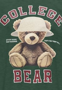 Groene stof met een grote, zachte teddybeer die een gestructureerde witte emmerhoed draagt. De tekst luidt "COLLEGE BEER" en "STUDY HARD NAP HARDER."