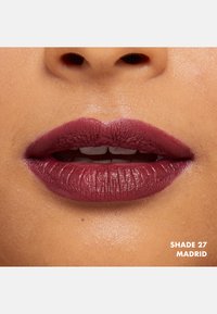Burgundy matt läppstift applicerat på läpparna, med en slät textur och en lätt glans, märkt som nyans 27 Madrid.