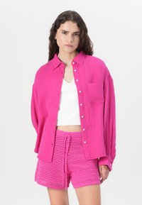 Camicia fucsia con bottoni e tasca, dal taglio rilassato, abbinata a pantaloni corti all'uncinetto fucsia con vita elastica.
