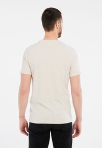 Jasbeżowa koszulka z krótkim rękawem i okrągłym dekoltem. Miękka tkanina, dopasowany krój oraz subtelna faktura. Noszona z ciemnymi, czarnymi dżinsami.