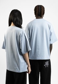 Light blue oversized t-shirts with dropped shoulders, made from soft fabric. One shirt features a spiderweb embroidery on black pants.