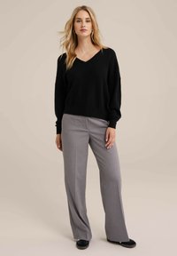Maglione nero a maglia con scollatura a V e maniche ampie, abbinato a pantaloni grigi su misura con gamba dritta e morbido tessuto. Scarpe nere.
