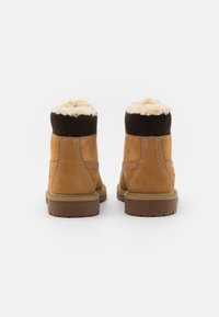 Stivali in suede marrone con un morbido rivestimento color crema e un colletto marrone scuro, dotati di una suola in gomma testurizzata e cuciture decorative.