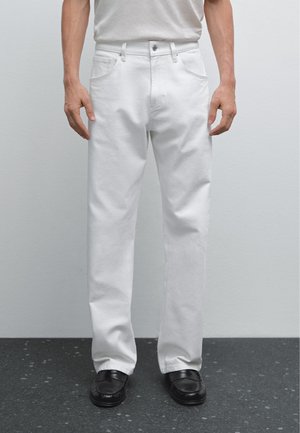 Witte katoenen broeken met een rechte pasvorm, voorzien van zijzakken, metalen knoopsluiting en een minimalistisch ontwerp. Platte, zwarte schoenen.