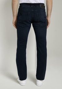 Tmavě modré džíny z denimu se slim fit střihem, designem s pěti kapsami a kontrastním prošitím. Mají koženou nášivku na zadním pase.