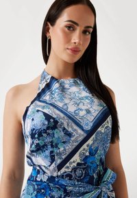 Top fără mâneci, tip halter, în imprimeu floral albastru, cu un amestec de nuanțe de albastru închis și deschis, modele intricate și un detaliu cu talie legată.