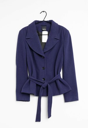 Marineblauwe damesblazer met brede revers, drie zwarte knopen, lange mouwen en een geknoopt stoffen ceintuur in de taille, hangend aan een zwarte hanger.