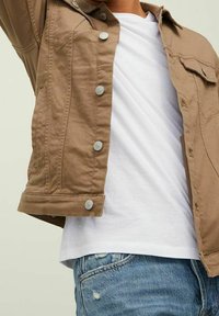 Brun denimjacka med silverknappar, med krage och bröstficka, bärs över en vit t-shirt och ljusblå slitna jeans.
