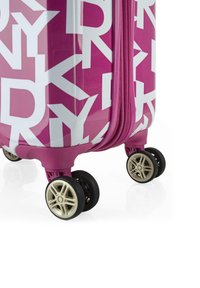 Maleta rígida de color rosa brillante con texto blanco. Cuenta con ruedas dobles y una superficie texturizada. Cierre de cremallera con ribete rosa a juego.