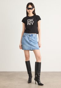 Schwarzes, verkürztes T-Shirt mit funkelnden "DK NY"-Buchstaben, kombiniert mit einem hellblauen Denim-Minirock und knielangen schwarzen Stiletto-Stiefeln.