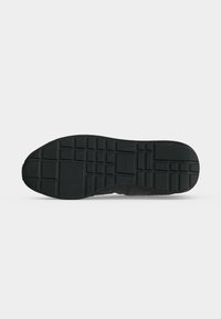 Semelle de chaussure noire avec motifs de bande de roulement carrés et rectangulaires, vue de dessous sur fond blanc.