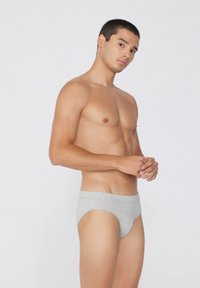 Szare bawełniane slipy o gładkiej fakturze, niskim kroju i szerokiej gumce w talii. Model stoi w profilu na jasnym tle.