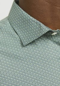 Camicia azzurro chiaro con piccolo motivo geometrico bianco, dotata di colletto a punte e tasca. Tessuto texture con finitura liscia.
