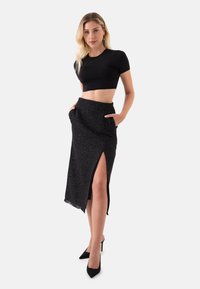 Zwarte cropped top gecombineerd met een gestructureerde zwarte midi-rok met een zijspleet en zakken, gedragen met zwarte pumps met spitse neuzen.