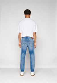 Blå denimjeans med avslappnad passform och blekningsdetaljer, kombinerat med en enfärgad vit t-shirt och vita sneakers. Enkelt design, inga mönster.