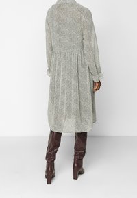 Vestido largo de color gris claro con estampado de pata de gallo y una falda acampanada, combinado con botas de cuero burdeos hasta la rodilla. Presenta un cuello y puños abotonados.