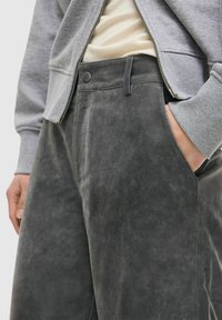 Grijze suède broek met wijde pijpen, voorzien van een voorzak, een gladde textuur en een bijpassende grijze trui die gedeeltelijk zichtbaar is.