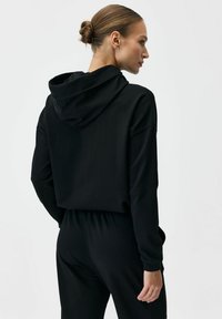 Czarna krótka bluza z kapturem ze sznurkiem, miękka tkanina, luźny krój oraz bezszwowy tył, zestawiona z czarnymi spodenkami z elastycznym pasem.
