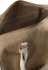 Beige getextureerde handtas met ritssluiting, voorzien van een crèmekleurige leren band en goudkleurige accenten. Binnenin bevindt zich een zakje en een logodetail.