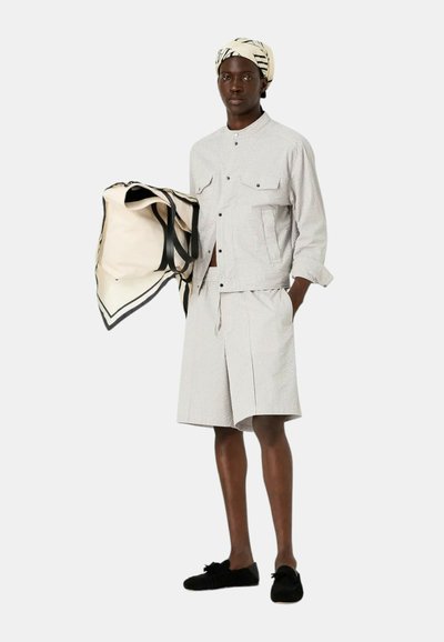 Camicia a righe chiare a maniche corte e pantaloni corti abbinati in grigio chiaro. Una borsa beige con manici neri e una sciarpa a fantasia completano il look.