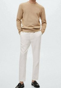 Beige gebreide trui, witte op maat gemaakte broek en zwarte loafers. Soepele texturen, aansluitend ontwerp en een ontspannen silhouet.