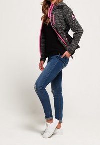 Veste à motif gris et noir avec accents rose, jean bleu slim fit avec détails usés, et baskets blanches portés ensemble.
