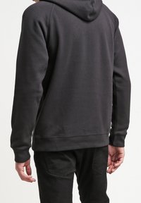 Svart, huvtröja tillverkad av mjukt tyg. Har ribbade muddar och nederkant, med en minimalistisk design utan synliga logotyper eller mönster.