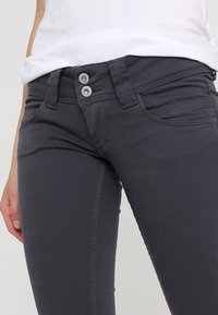 Šedé džíny s slim fit střihem, s dvojitým zapínáním, předními kapsami a tónovým prošíváním pro zvýraznění detailů.