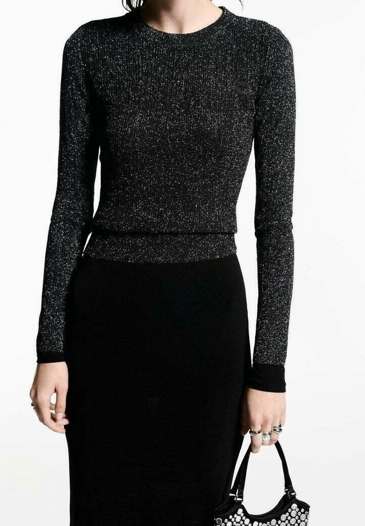 Schwarzes Langarmoberteil aus texturiertem, glitzerndem Stoff. Geripptes Design am Ausschnitt und an den Bündchen. Kombiniert mit einem eng anliegenden schwarzen Rock und einer kleinen Handtasche.