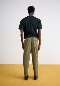 Fekete pamut póló és olíva zöld, elasztikus derekú, slim fit nadrág oldalzsebekkel, sárga padlón.