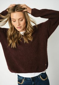 Bordeaux oversized gebreid sweater met een zachte, textuurafwerking, met verlaagde schouders en een afgeronde zoom, gecombineerd met blauwe jeans.