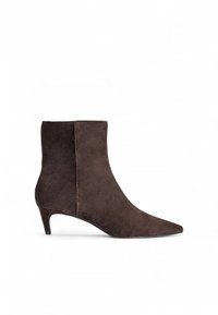 Bottine en daim marron avec un bout pointu, une silhouette courbée et un talon bas, présentant une texture lisse et un design minimaliste.