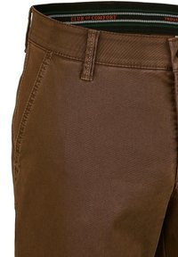 Braune Hose aus glattem Stoff mit einem gewebten Bund, der die Marke "CLUB OF COMFORT" trägt, detaillierter Nahtführung und klassischem Schnitt.