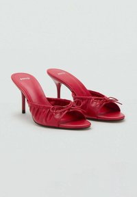 Mules à talons rouges avec une finition en cuir brillant, bout ouvert et design froncé. Présentent un détail en nœud et un talon aiguille élégant.
