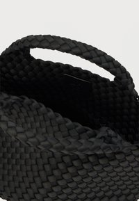 Μαύρη υφασμάτινη τσάντα καλαθιού με λεία υφή, διαθέτει πλεκτή λαβή και ετικέτα στο εσωτερικό. Συμπαγής σχεδιασμός κατάλληλος για διάφορες χρήσεις.