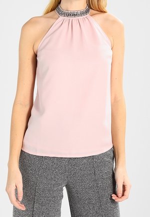 Femme portant un haut rose clair sans manches à col licou orné de perles, associé à un pantalon gris texturé.