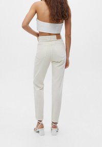 Top cortado blanco, jeans crema de cintura alta con cinco bolsillos y sandalias blancas de tacón bloque con tiras. Diseño minimalista y ajustado.
