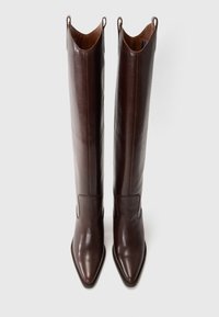 Botas de cuero marrón hasta la rodilla con punta afilada y bucles dobles distintivos en la parte superior, que presentan una textura suave y un diseño elegante.