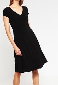 Robe noire à manches courtes avec un décolleté en V, fabriquée en tissu doux, présentant une jupe évasée et des poches latérales pour plus de fonctionnalité.