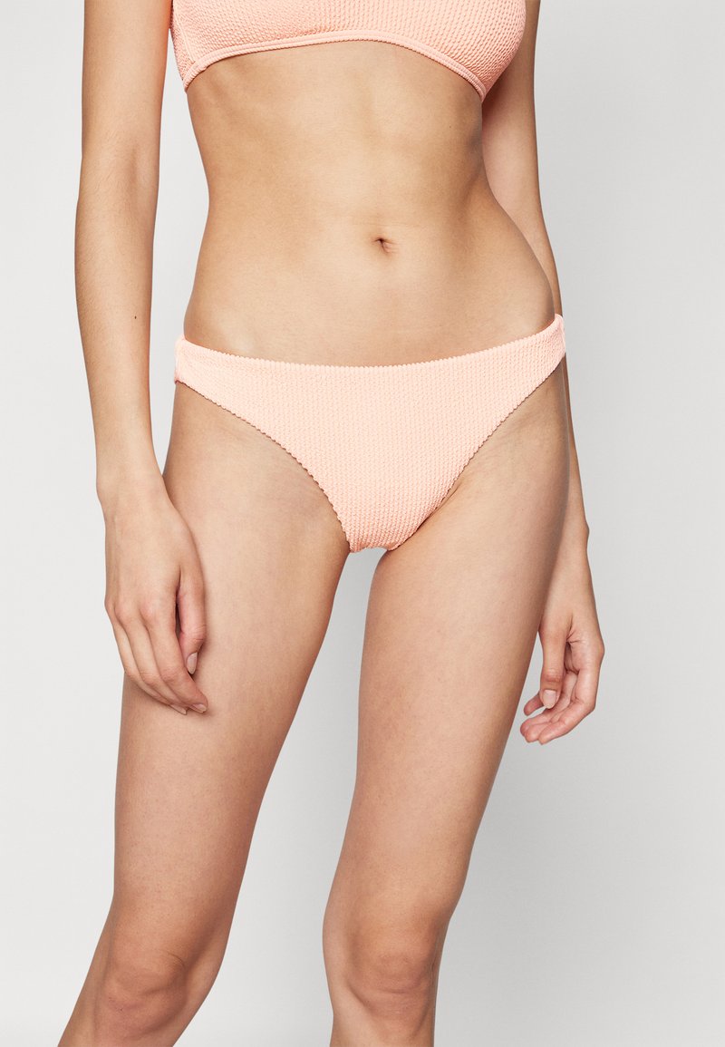 Bas de bikini en texture pêche avec une taille basse et une ceinture élastique, présentant des coutures subtiles le long des bords.