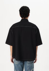 Juodas trumpas rankovėmis marškinėliai su taškais apykakle, su kontrastingomis baltomis siūlėmis, pagaminti iš lygaus audinio.