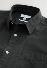 Čierna slim-fit košeľa vyrobená z tkaniny. Obsahuje golier na gombíky, predné vrecko a biele gombíky. Viditeľná etiketa so značkou a veľkosťou.