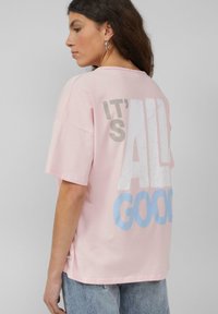 Roze katoenen t-shirt met een relaxte pasvorm, met grote witte en blauwe tekst op de achterkant met de tekst "IT'S ALL GOOD." Korte mouwen.
