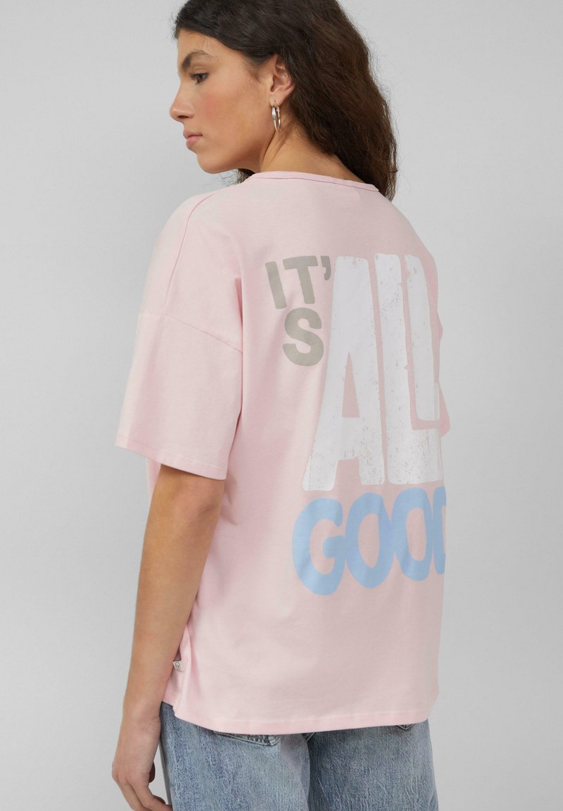 Roze katoenen t-shirt met een relaxte pasvorm, met grote witte en blauwe tekst op de achterkant met de tekst "IT'S ALL GOOD." Korte mouwen.