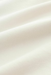 Biała bawełniana tkanina o gładkiej fakturze, z delikatnymi fałdami oraz miękkim, równym splotem. Bez widocznych wzorów ani akcentów.