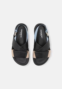 Sandale negre din piele cu curele încrucișate, cu un accent bleu deschis și o cataramă aurie. Talpa plată, textură netedă, design minimalist.