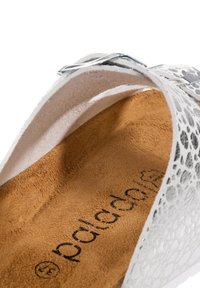 Vit sandal med silverfästen och texturerad innersula som visar varumärket "padders" på en mjuk brun fotbädd.