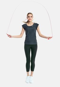 Gray athletic top and black leggings with a fitted design. The individual is holding a red jump rope, standing on white sneakers.