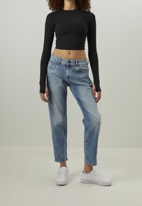 Black long-sleeve crop top paired with light blue, relaxed-fit denim jeans and white sneakers, showcasing a casual, layered outfit.